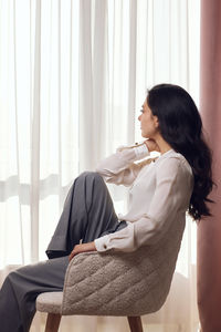 Young woman using mobile phone while sitting on bed at home