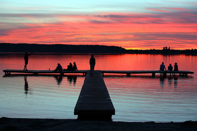 Silhouette people by lake on jetty during sunset