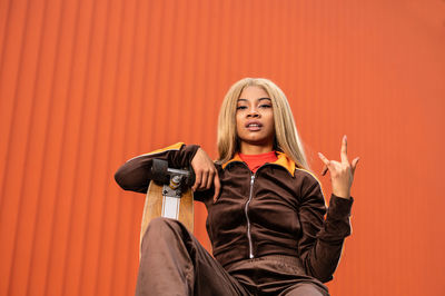 Young african american woman with long blonde hair and sportswear on an orange background