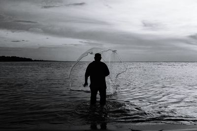 Rear view of silhouette man fishing in sea against sky