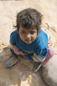 High angle portrait of girl wearing warm clothing while sitting on sand