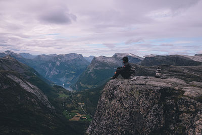 Side view of man sitting on mountain against sky