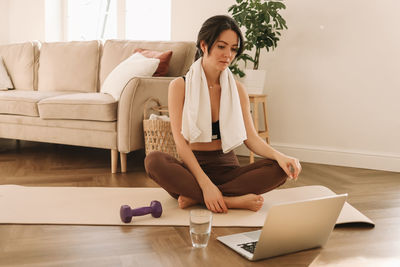 Fitness girl looks at her laptop while doing sports training and physical activity at home