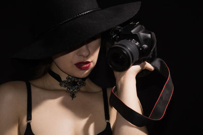 Close-up of young woman holding camera over black background