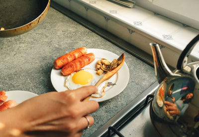 Cooking lovely breakfast set of sausages and fired egg in the kitchen in warm morning light.