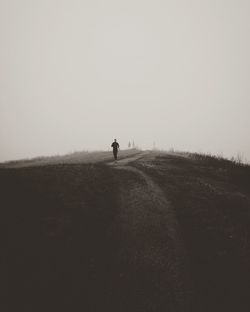 Rear view of man walking on field against clear sky