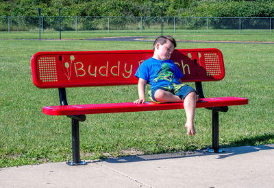 A sad lonely little boy sits on a buddy bench waiting for a friend to notice he is alone