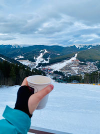 Midsection of person holding coffe against mountains