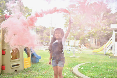 Portrait of happy girl holding distress flare while standing on grassy field at playground