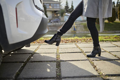 Woman opening car trunk with foot sensor on footpath