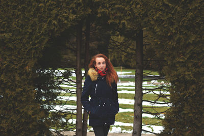 Portrait of smiling young woman standing against trees during winter