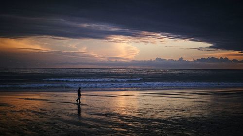 Silhouette man standing on beach against sky during sunset