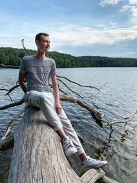 Young woman sitting by lake against sky
