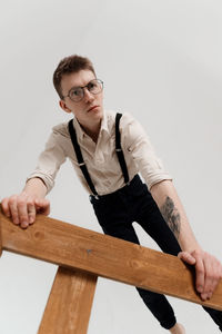 Portrait of young man with ladder standing against white background