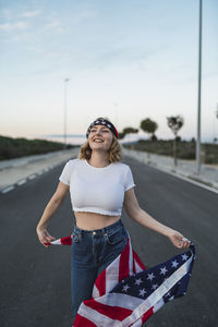 Young woman wearing sunglasses standing on road against sky