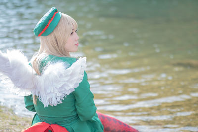 Side view of woman in angel costume sitting by lake