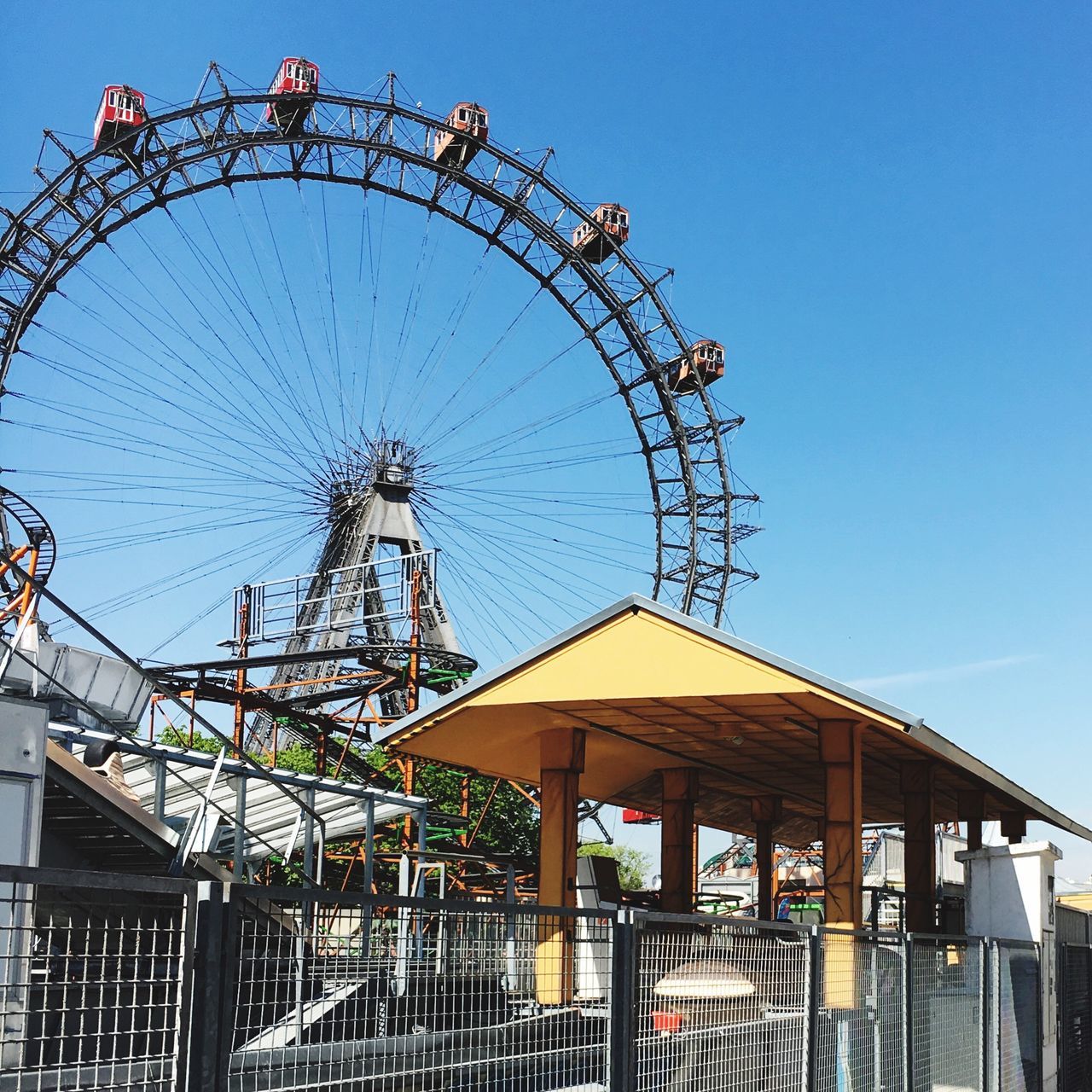 ferris wheel, amusement park, amusement park ride, arts culture and entertainment, built structure, low angle view, architecture, building exterior, sky, clear sky, blue, metal, outdoors, day, circle, big wheel, no people, large, city, fairground ride