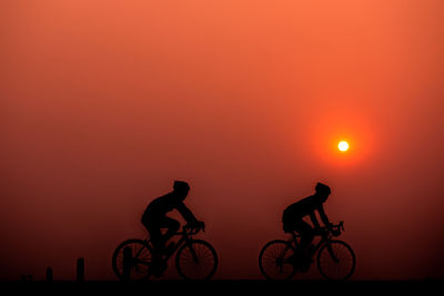 Silhouette bicycles against orange sky