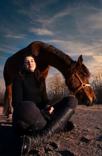 Woman sitting with horse on field