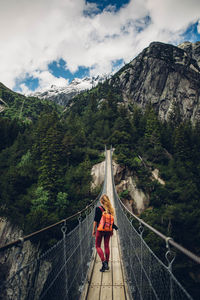 Rear view of woman standing on footbridge in forest