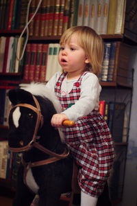 Cute girl looking away while sitting on rocking horse at home