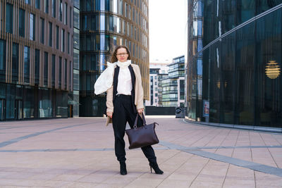 Successful woman with glasses stands in front of an office building with bag