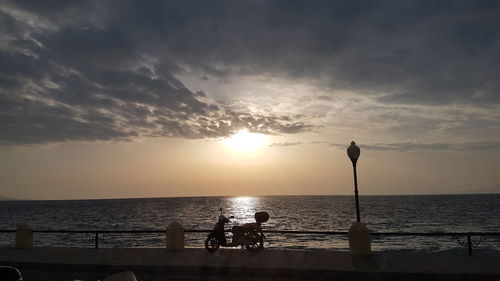 Silhouette people on sea against sky during sunset