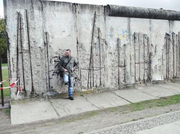 Man holding umbrella on footpath against wall