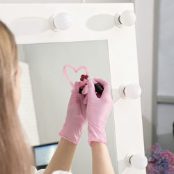 Woman wearing medical gloves drawing a heart with lipstick on a mirror. beauty cosmetology 