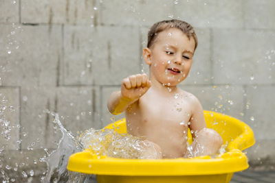 Cute little boy bathing in yellow tub outdoors. happy child is splashing, playing with water