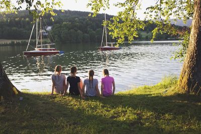 Rear view of people sitting on lake against sky