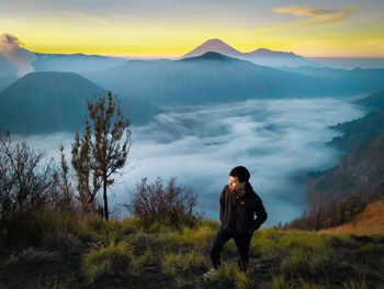 Full length of young woman standing on land against sky during sunset