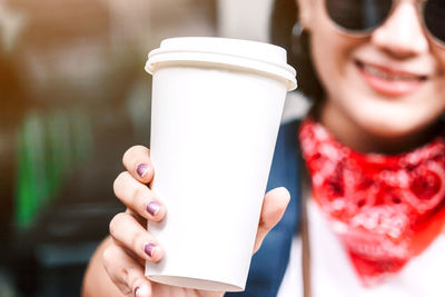 Close-up of young woman holding disposable cup in city