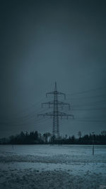 Electricity pylon on snow covered field against sky