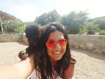 Portrait of smiling young woman wearing sunglasses against sky