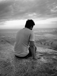Rear view of man sitting on landscape against sky