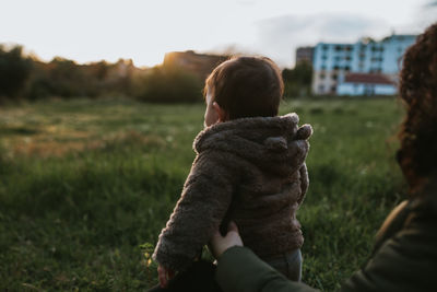 Rear view of mother and daughter on grass against sky