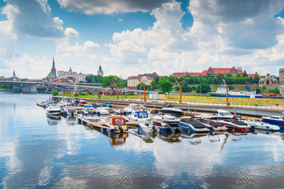 Boats moored at harbor against sky in city