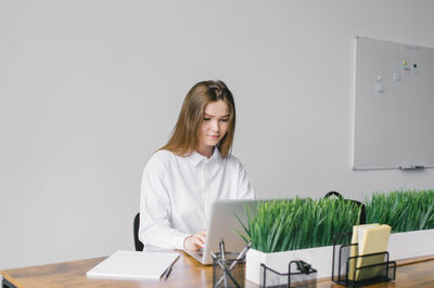 A cute girl is sitting at a wooden desk in the office working with a laptop