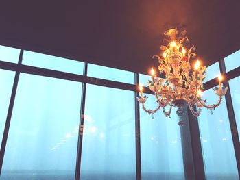 Low angle view of illuminated chandelier by window