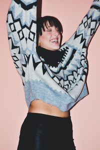 Cheerful young woman with arms raised standing against wall