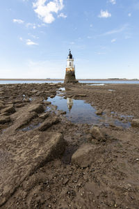 Lighthouse on beach by sea against sky