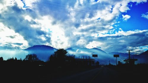 Road amidst silhouette trees against sky