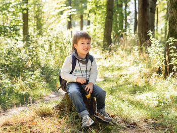 Little explorer on hike in forest. boy with binoculars sits on stump. summer journey for tourist.