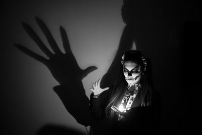 Portrait of spooky woman standing with illuminated lighting equipment in darkroom