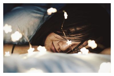 Close-up of woman lying with illuminated string lights on bed