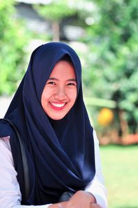 Portrait of cheerful young woman wearing hijab against trees