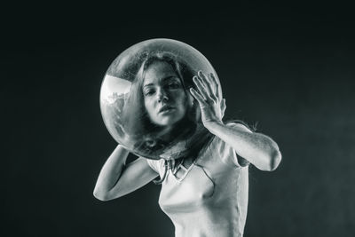 Young woman wearing glass container against black background