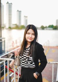 Portrait of young woman standing against railing