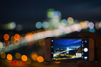 Cropped hand holding phone against city at night